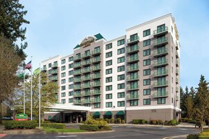 A multi-story hotel with a central entrance, balconies on each floor, and a clear sky.