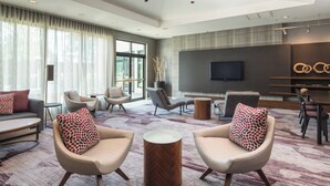 A modern hotel lobby with a large seating area, a flat-screen TV mounted on the wall, and a dining area with a wooden table and chairs. - Courtyard by Marriott Seattle Federal Way (Federal Way)