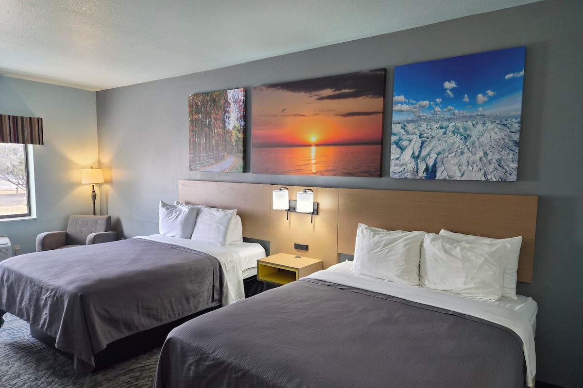 A hotel room with two beds, a desk, a chair, and wall art depicting nature scenes.