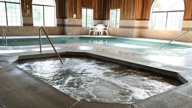An indoor swimming pool with a hot tub area, wooden walls, and a table with chairs.