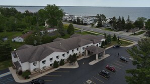 A coastal hotel with a parking lot, a marina in the background, and a view of the sea.
