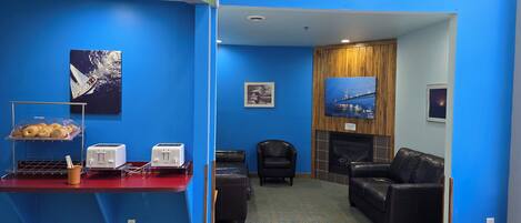 A room with blue walls, a red counter with a toaster, a coffee cup, and a tray of pastries. There is a black leather couch and a fireplace in the background.