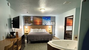 A hotel room with a bed, a desk with a chair, a large bathtub, and wall-mounted artwork.