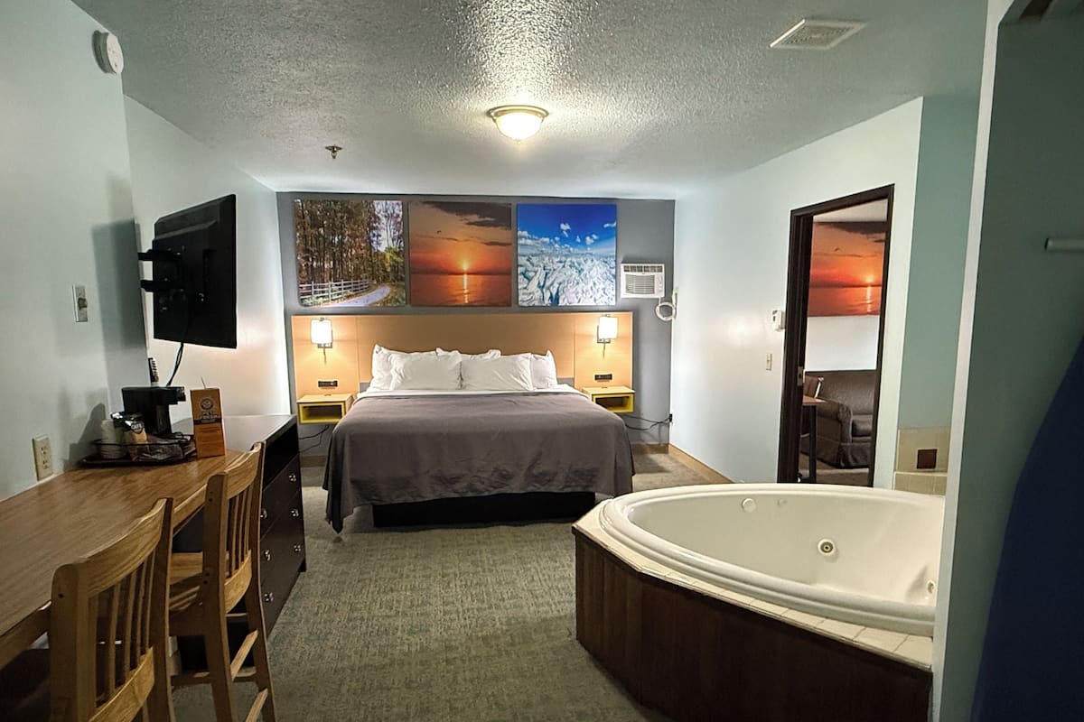 A hotel room with a bed, a desk with a chair, a large bathtub, and wall-mounted artwork.