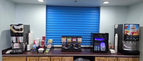 A coffee station with multiple coffee machines, a beverage dispenser, and a trash bin.