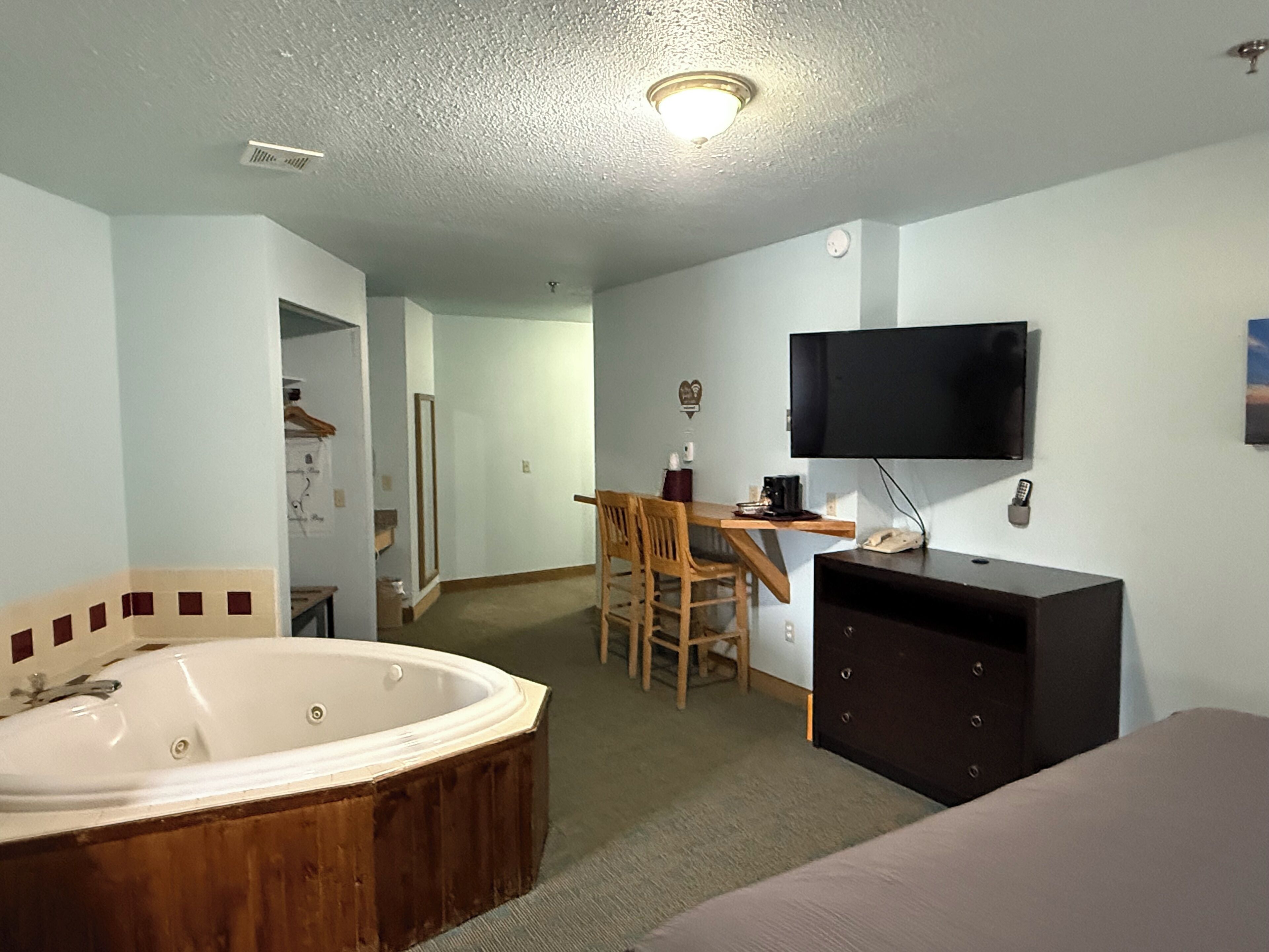 Una habitación con una bañera grande, un escritorio con silla, televisor y cómoda.