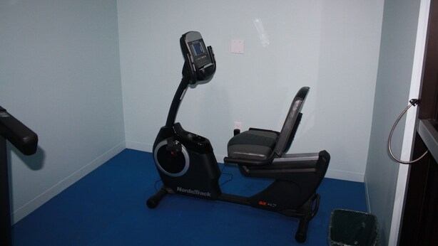 A small room with a NordicTrack exercise bike, a blue carpet, and a white wall. - Bay Inn (Tawas City)