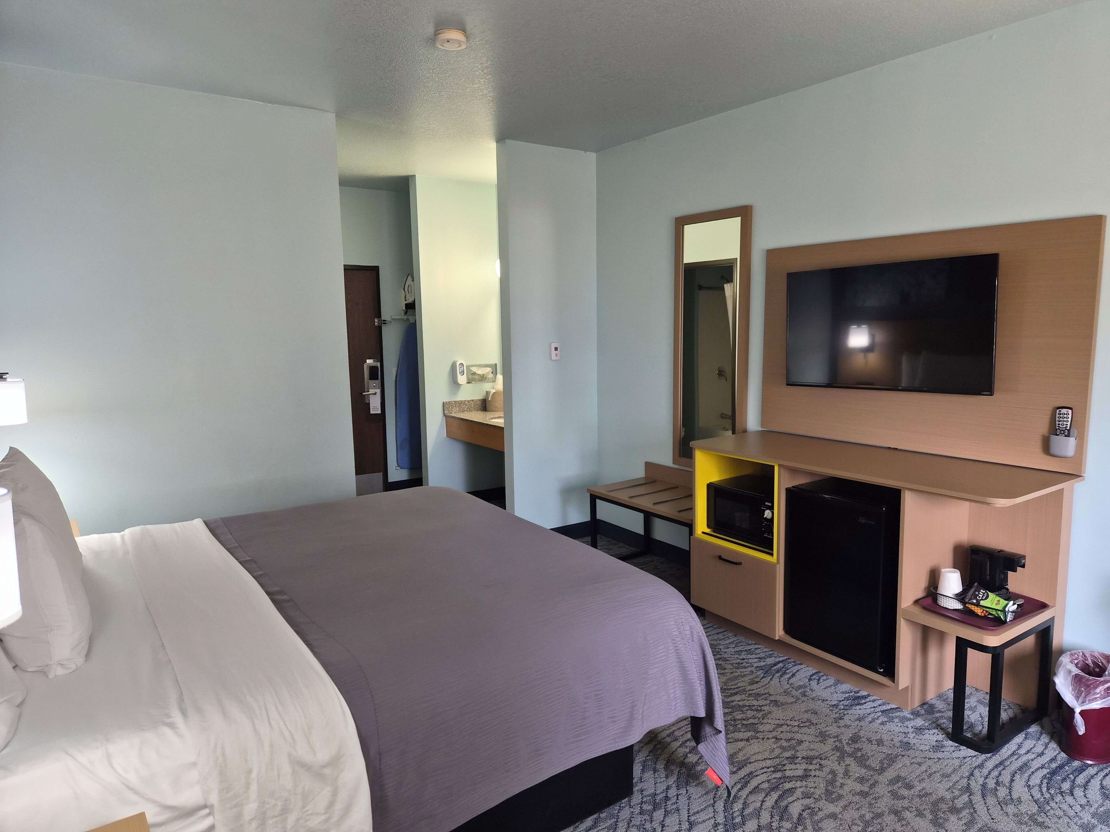 Une chambre d’hôtel équipée d’un lit, d’une télévision, d’un bureau avec un miroir et d’un four à micro-ondes.