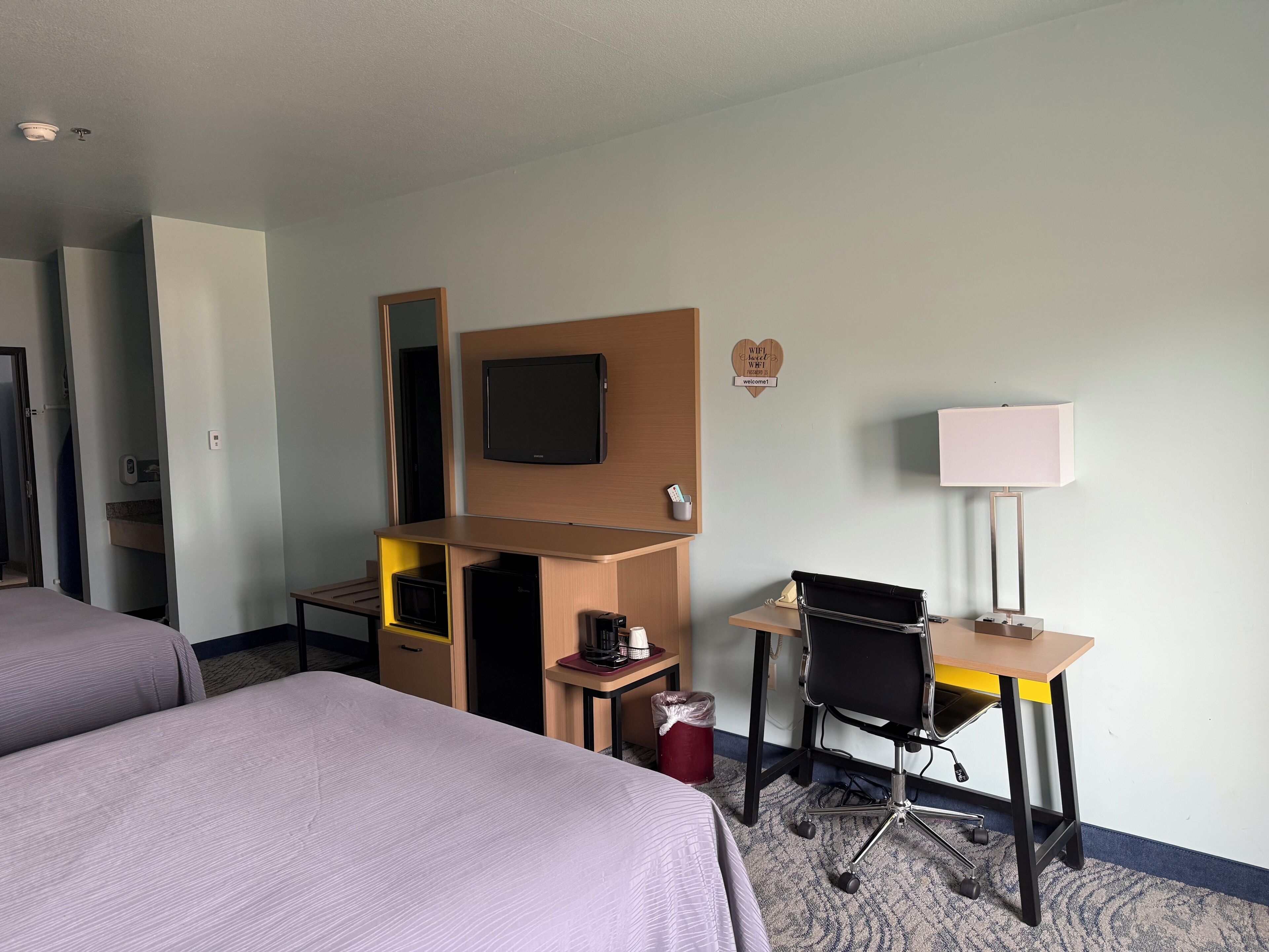 Habitación de hotel con dos camas, un escritorio con silla, televisor, cafetera y un cubo de basura pequeño.