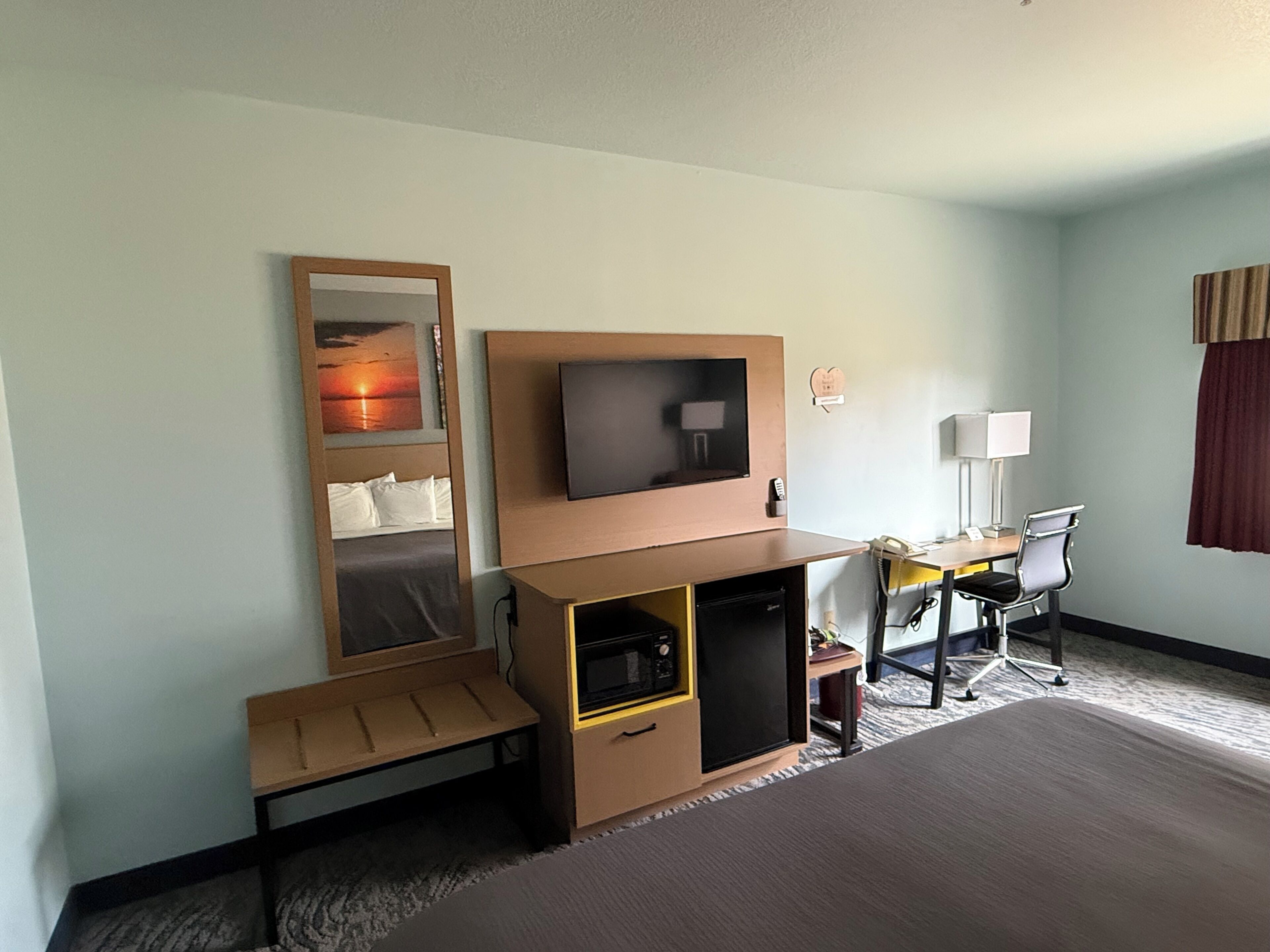 A hotel room with a bed, a desk with a chair, a television, a small cabinet, and a bedside table.