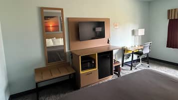 A hotel room with a bed, a desk with a chair, a television, a small cabinet, and a bedside table.