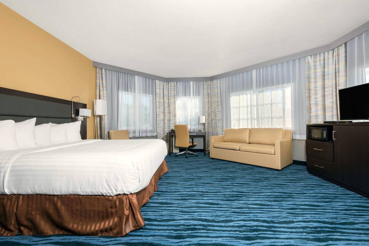 A hotel room with a large bed, a sofa, a desk with a chair, a television, and a wardrobe.