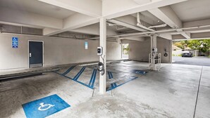 A parking garage with designated handicapped spaces, a charging station, and a security camera. - Hotel 1550 - SFO Airport (San Bruno)
