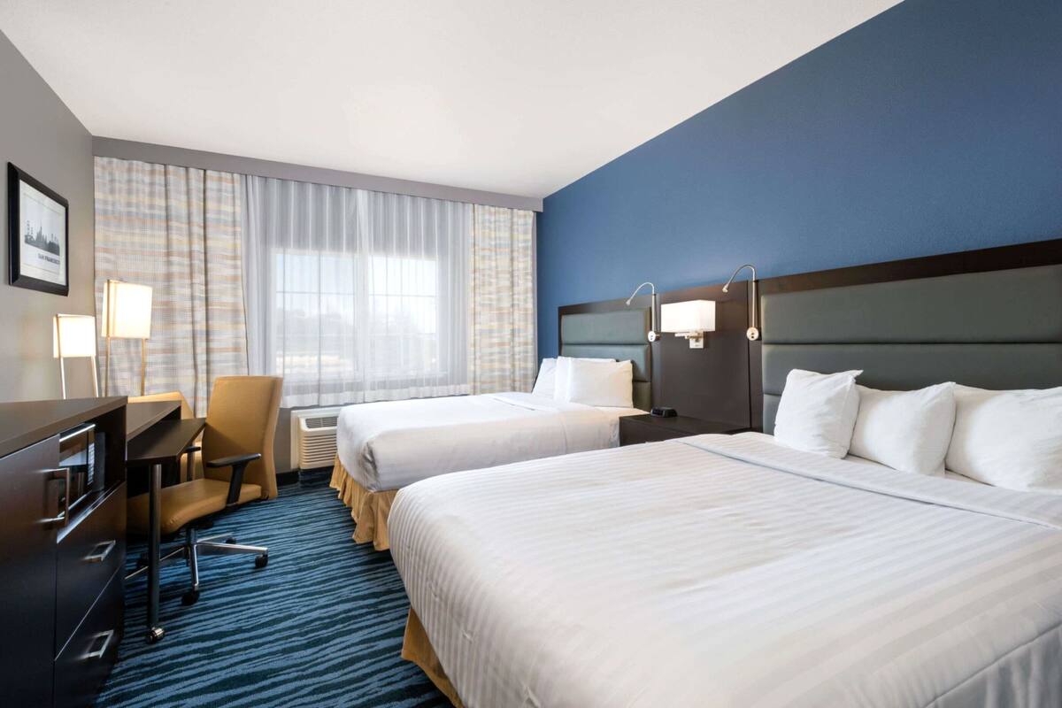A hotel room with two beds, a desk, a chair, and a large window with curtains.