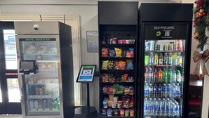 A self-service kiosk with a digital screen, a refrigerated snack vending machine, and a refrigerated beverage vending machine. - Hotel 1550 - SFO Airport (San Bruno)
