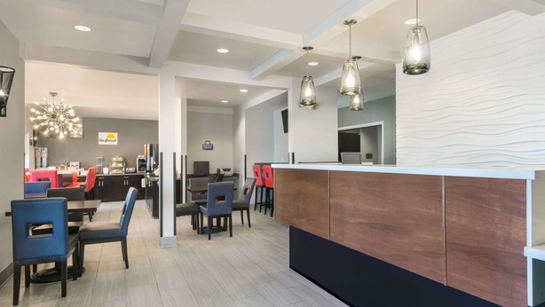 A modern hotel lobby with a reception desk, dining area with tables and chairs, and a decorative light fixture. - Hotel 1550 - SFO Airport (San Bruno)