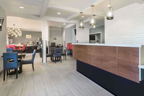 A modern hotel lobby with a reception desk, dining area with tables and chairs, and a decorative light fixture. - Hotel 1550 - SFO Airport (San Bruno)