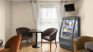 A room with a table, two chairs, a sofa, a television, and a Coca-Cola refrigerator.
