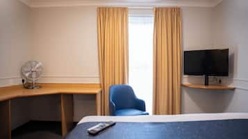 Habitación de hotel con cama, escritorio, silla, televisión y ventana con cortinas.