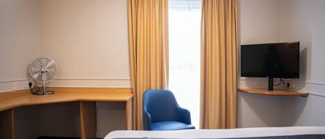 A hotel room with a bed, a desk, a chair, a TV, and a window with curtains.