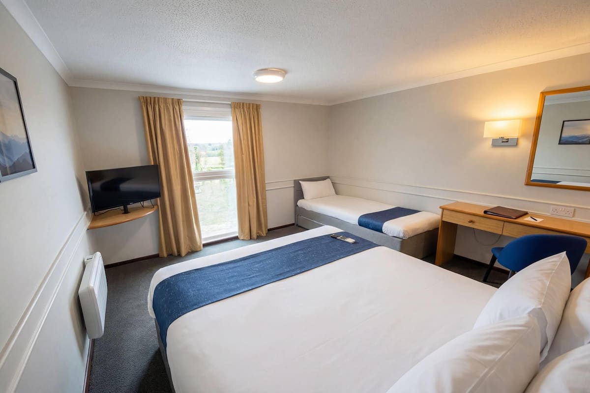 Een hotelkamer met twee bedden, een bureau, een stoel, een televisietoestel en een raam met gordijnen.