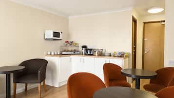 Cocina compacta con microondas, cafetera y un pequeño comedor con dos sillas y una mesa.