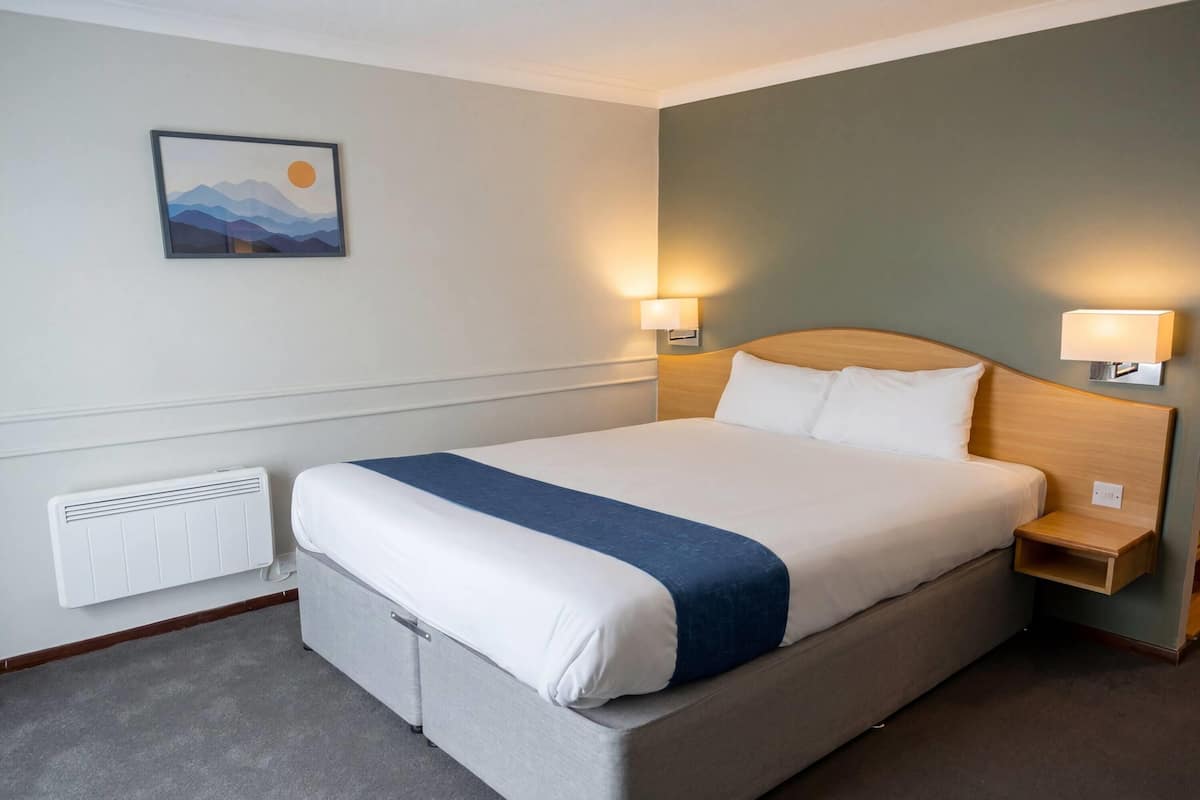 Een net opgemaakt bed met blauwe accenten, een aan de muur hangend schilderij en twee bedlampjes.