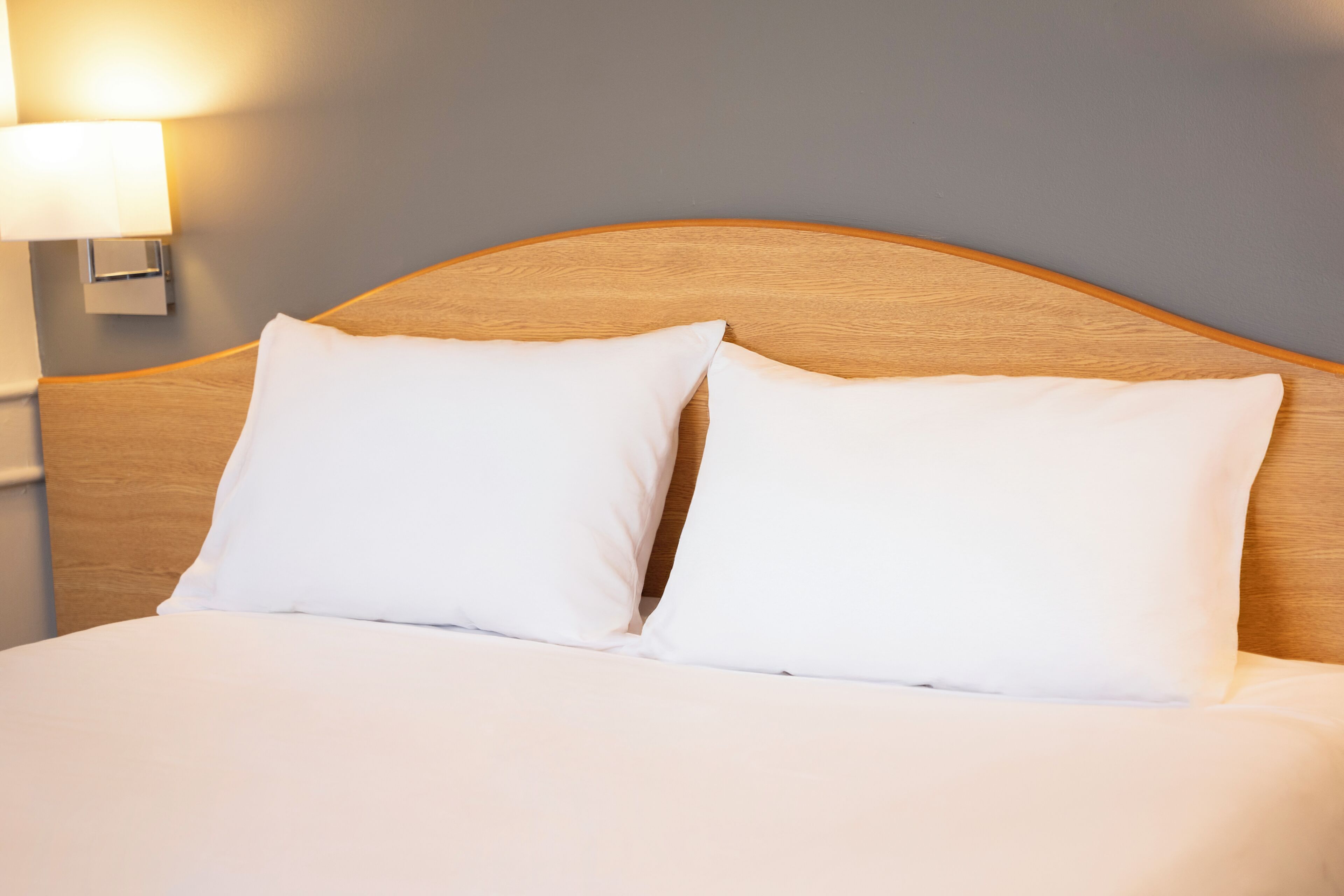 Una cama bien hecha con dos almohadas blancas y un cabecero de madera.