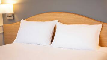 Una cama bien hecha con dos almohadas blancas y un cabecero de madera.