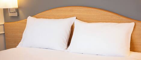 Una cama bien hecha con dos almohadas blancas y un cabecero de madera.