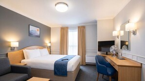 A hotel room with a bed, desk, chair, and a TV.