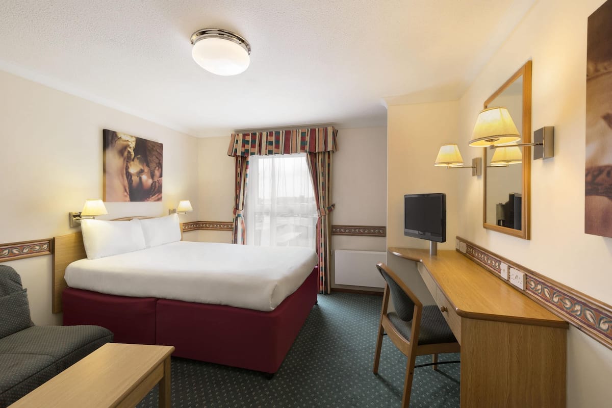 Een hotelkamer met een bed, bureau, stoel, televisie en een raam met gordijnen.
