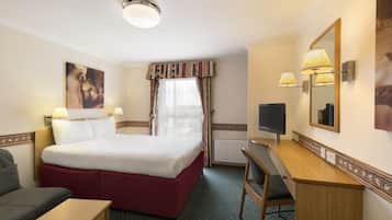 Une chambre d’hôtel équipée d’un lit, d’un bureau, d’une chaise, d’une télévision et d’une fenêtre avec des rideaux.