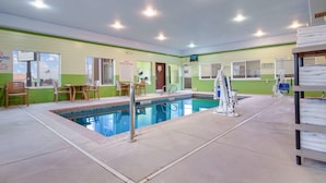 Un área de piscina interior con trampolín, sillas junto a la piscina y una mesa.