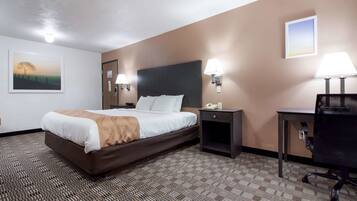 A hotel room with a large bed, a desk, a chair, a nightstand, and a wall-mounted lamp.