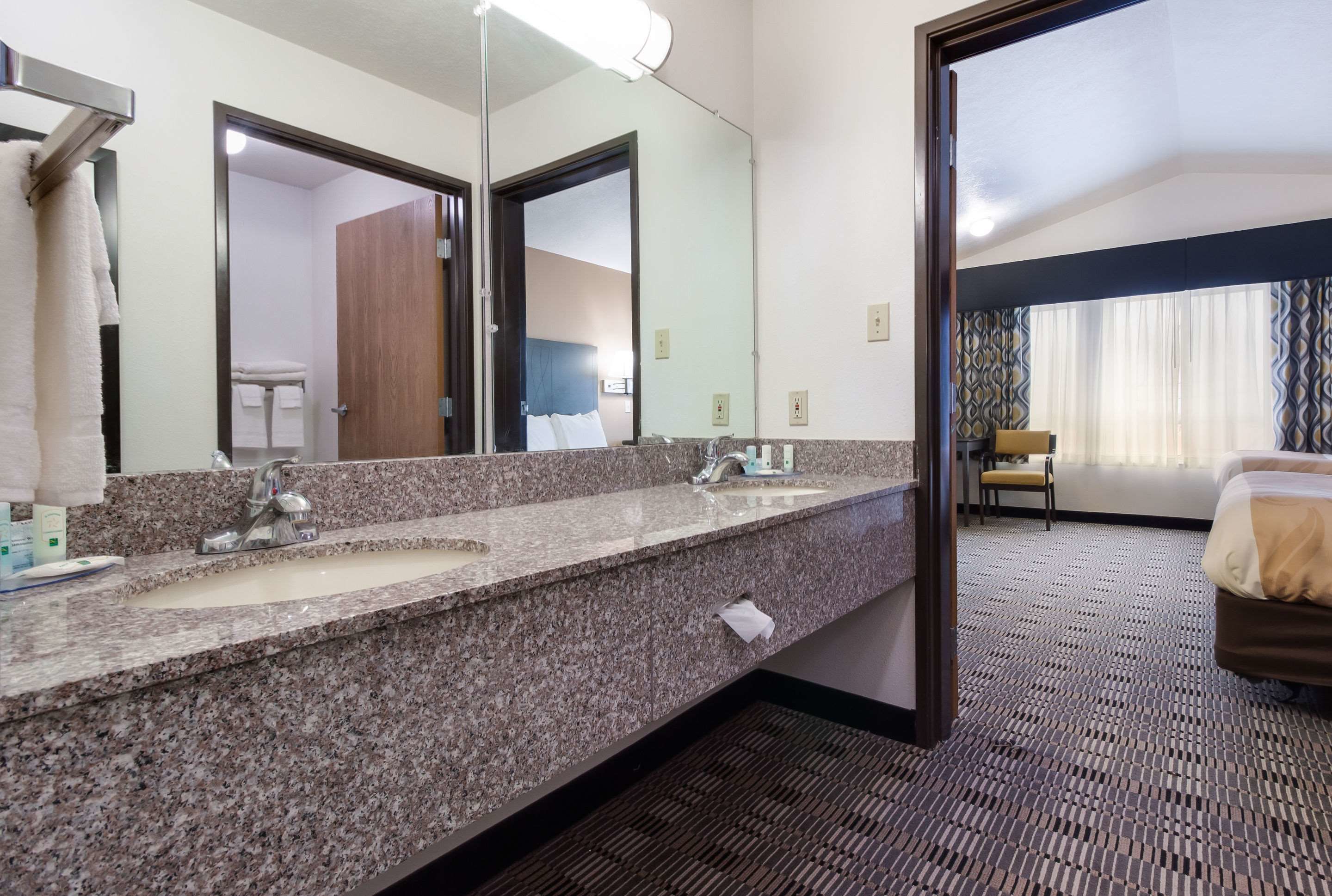 Un bagno d'albergo con due lavandini, uno specchio grande e una porta che dà su una camera da letto.