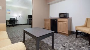 Habitación de hotel con kitchenette pequeña, un escritorio, una silla y alfombra estampada.