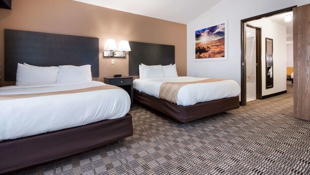 Habitación de hotel con dos camas, una mesita de noche con lámparas, un cuadro en la pared y una puerta de madera.