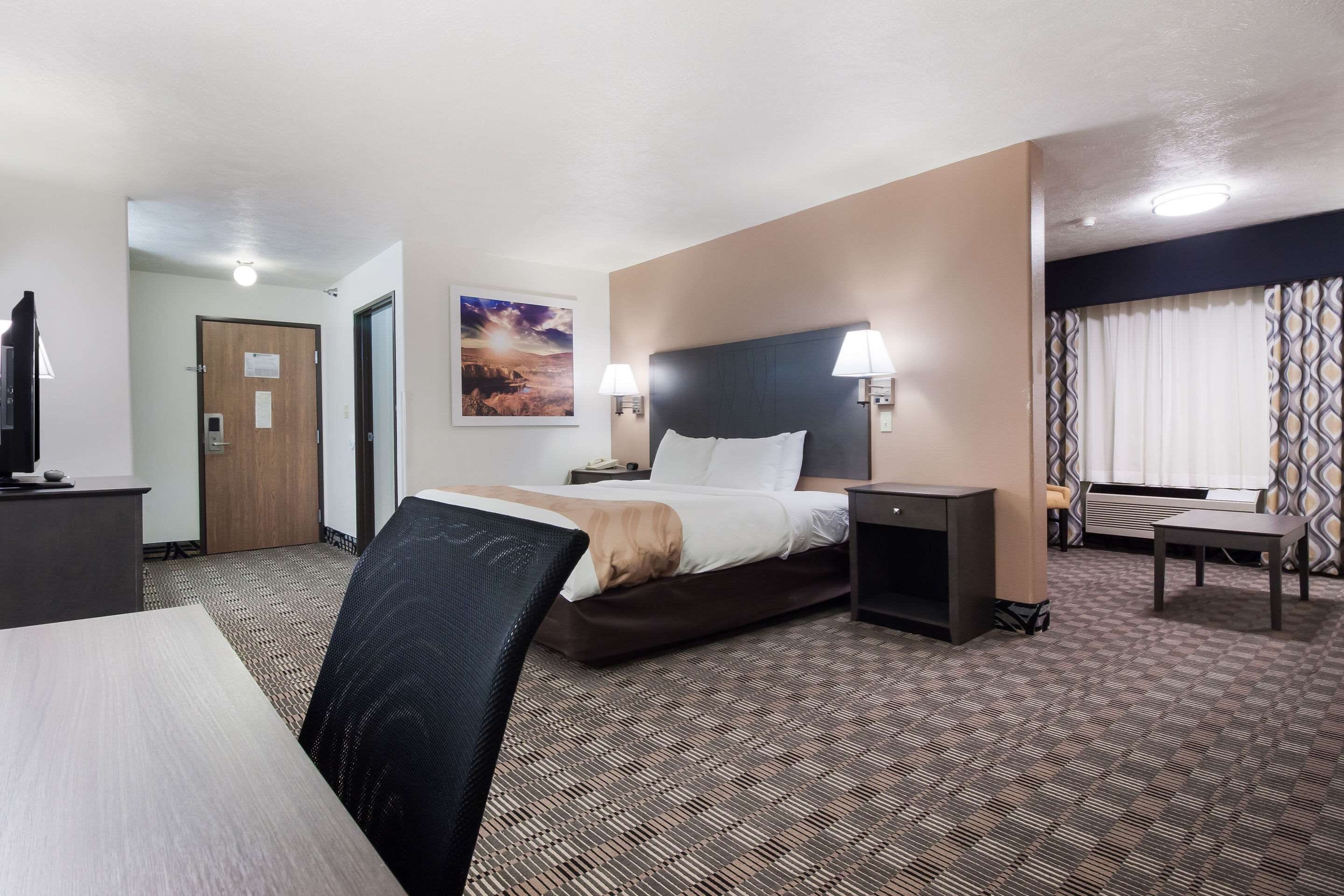 A hotel room with a bed, bedside tables, a desk, a chair, a TV, and a window with curtains.