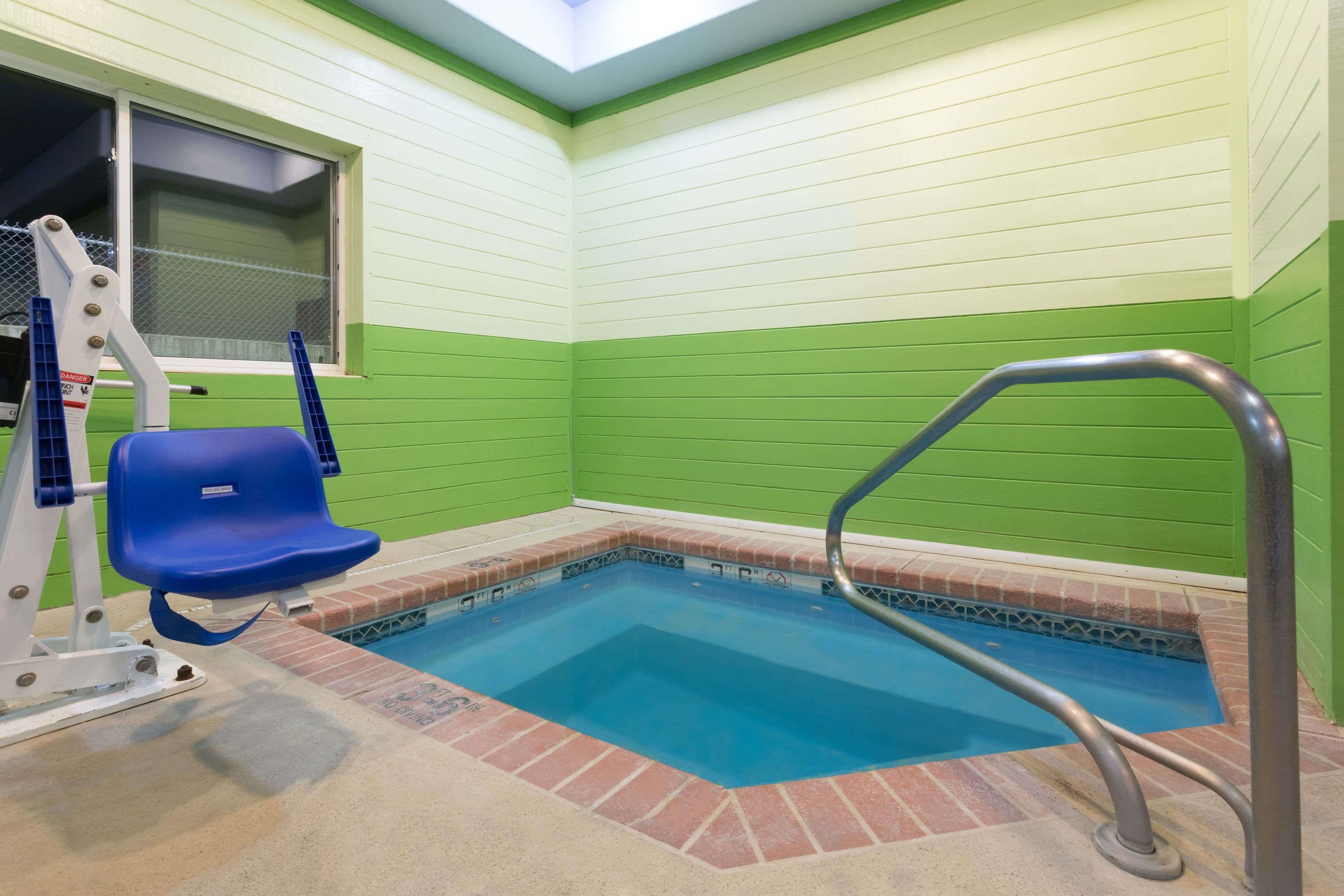 Una pequeña piscina interior con una fuente de agua azul, una silla azul y una barandilla de metal.