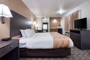 A hotel room with a bed, bedside table, lamp, TV, and a kitchenette area.