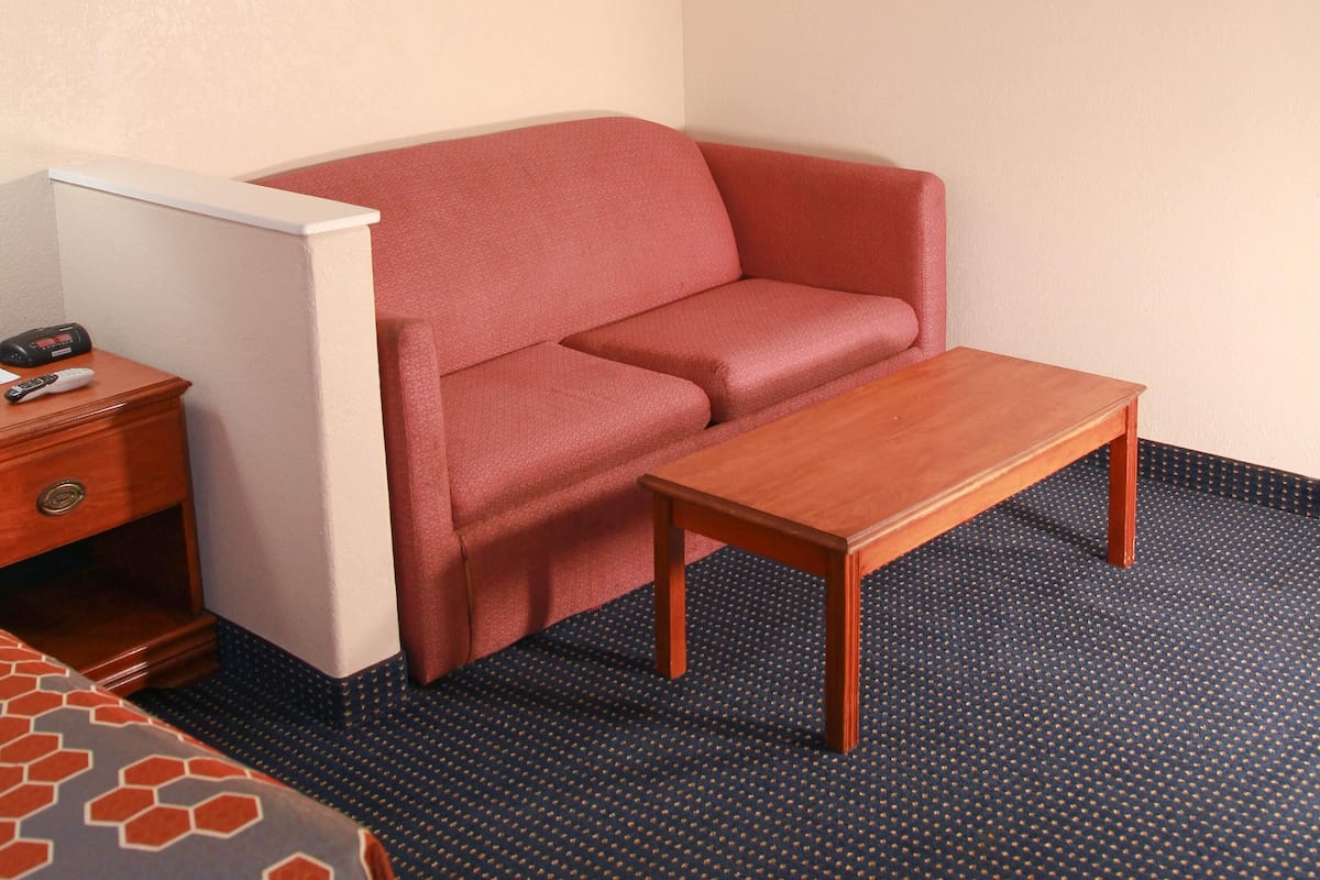 Quarto pequeno e acolhedor, com um sofá vermelho, uma mesa de madeira e uma mesa de cabeceira com controle remoto.