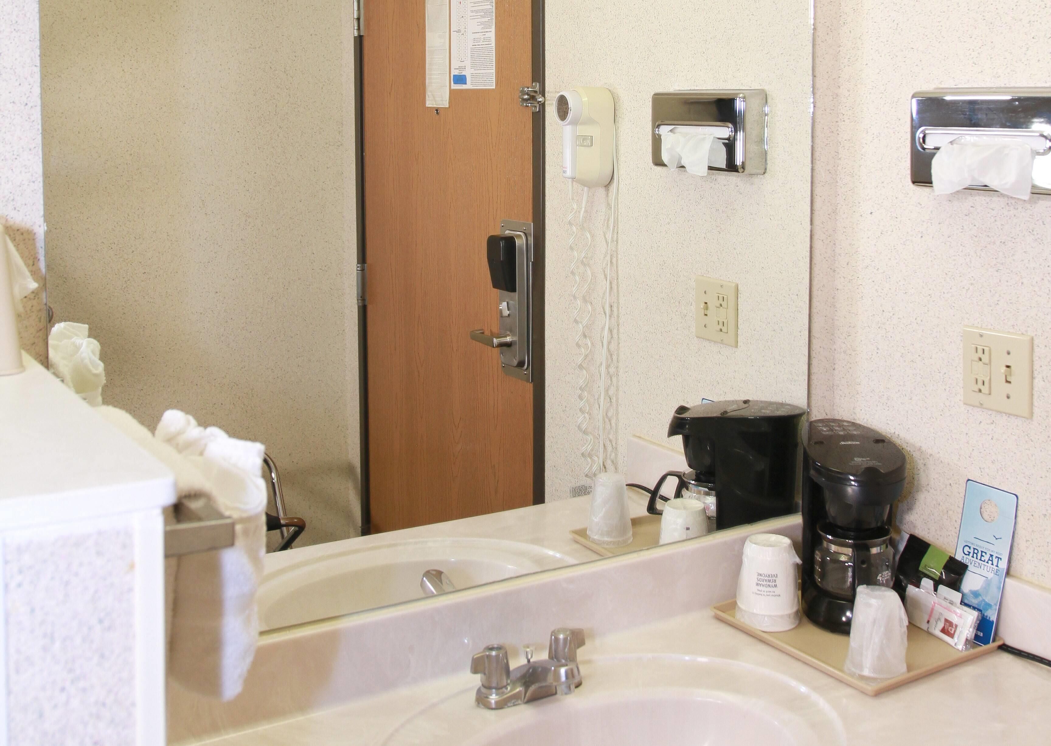 Un baño de hotel con lavamanos, espejo y artículos de aseo.