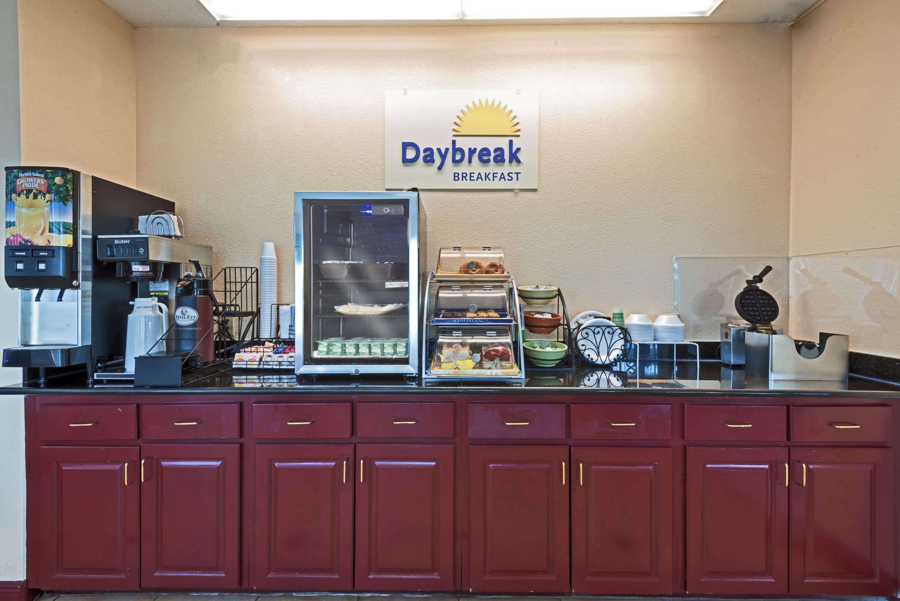 A breakfast counter with a sign reading "Daybreak Breakfast," coffee machines, a glass display case, and various food items.