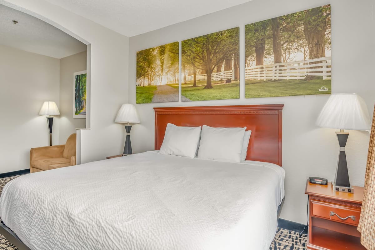 A hotel room with a large bed, two bedside lamps, a wooden nightstand, and three framed pictures on the wall.