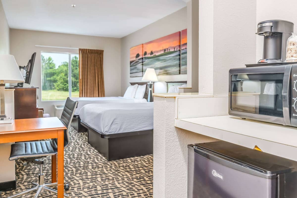 A hotel room with a bed, desk, chair, coffee maker, microwave, and a refrigerator.