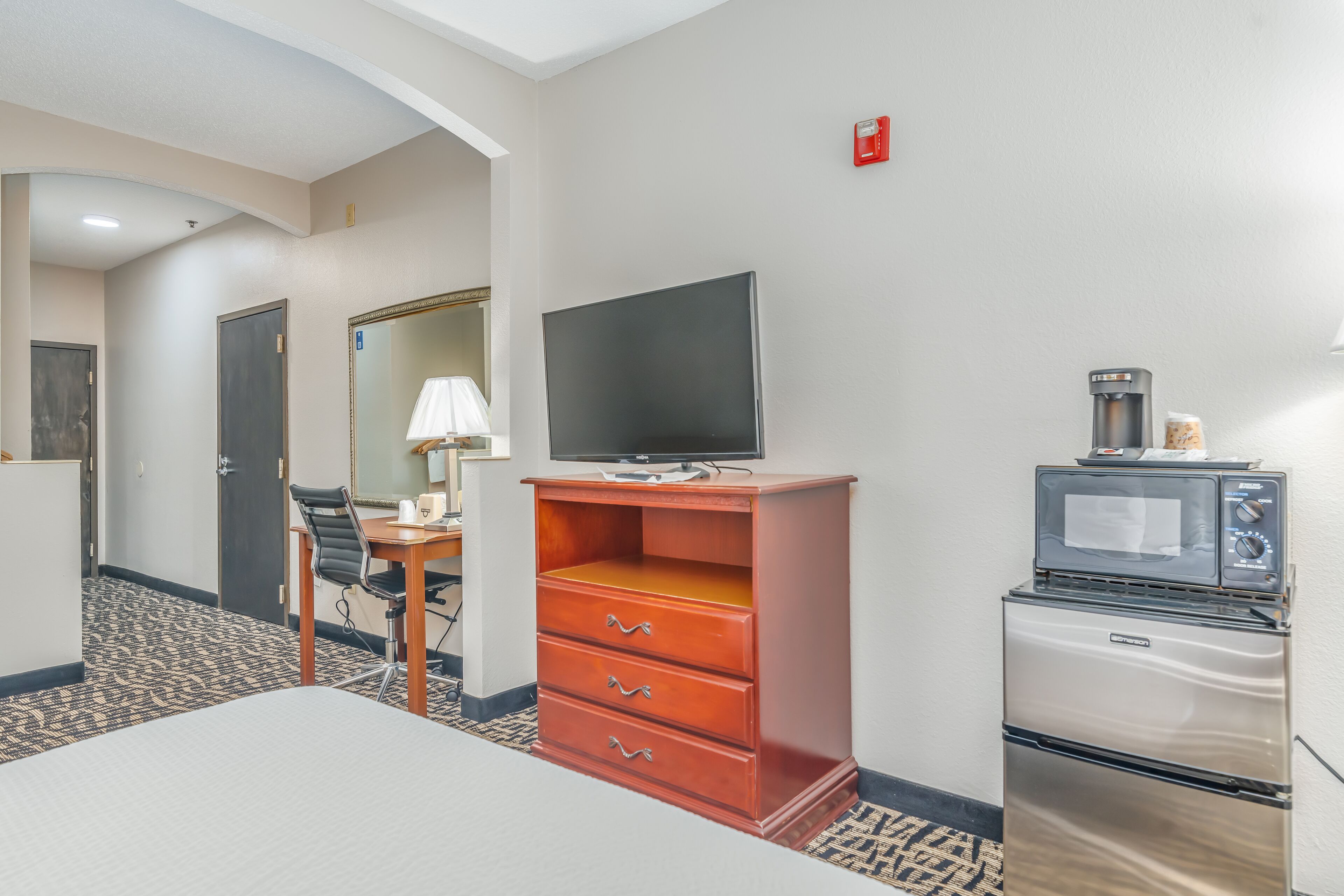 A hotel room with a bed, a desk with a chair, a television, a microwave, and a refrigerator.