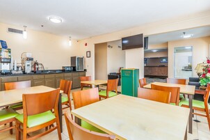 Un comedor de hotel con mesas y sillas de madera, una máquina de café y un televisor montado en la pared.