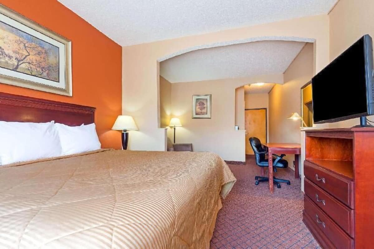 A hotel room with a bed, desk, chair, TV, and lamps.