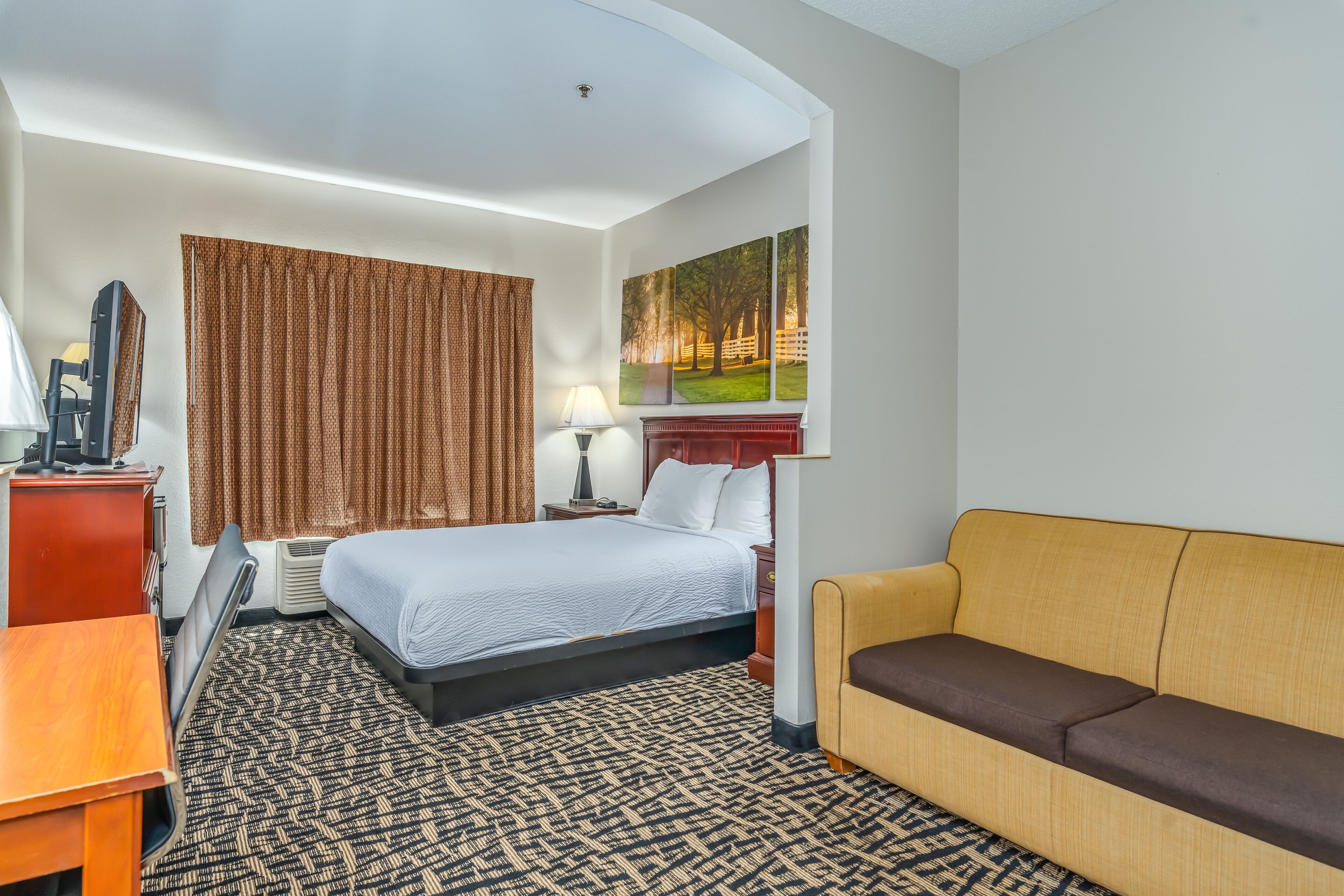 A hotel room with a bed, a sofa, a desk, a lamp, and a painting on the wall.